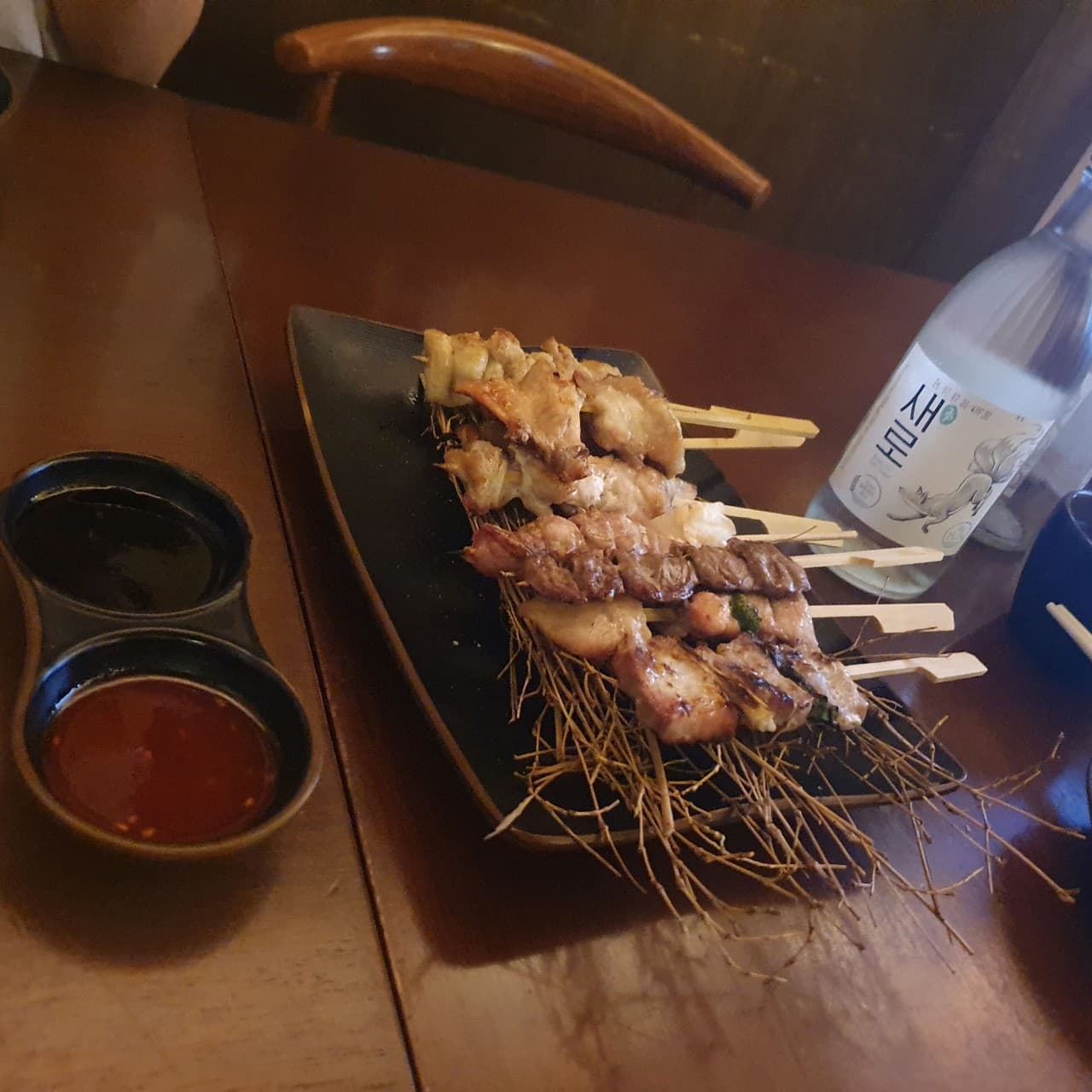 대구광역시 중구 이자카야미우 대구 이자카야 따뜻한 조명 아래 1인 다찌석에 차려진 꼬치 구이와 소주. 나무 테이블 위에서 정갈한 질감의 안주와 함께 혼술을 즐기는 상황.