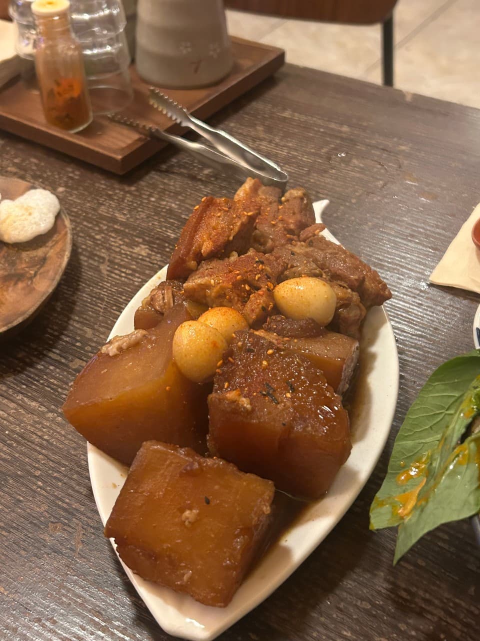 대구광역시 동구 요시쿠 신서 본점 대구 이자카야 다찌석 조명 아래 놓인 1인 혼술 안주. 윤기 나는 무와 돼지고기 조림이 나무 테이블 위에 정갈하게 차려진 상황.