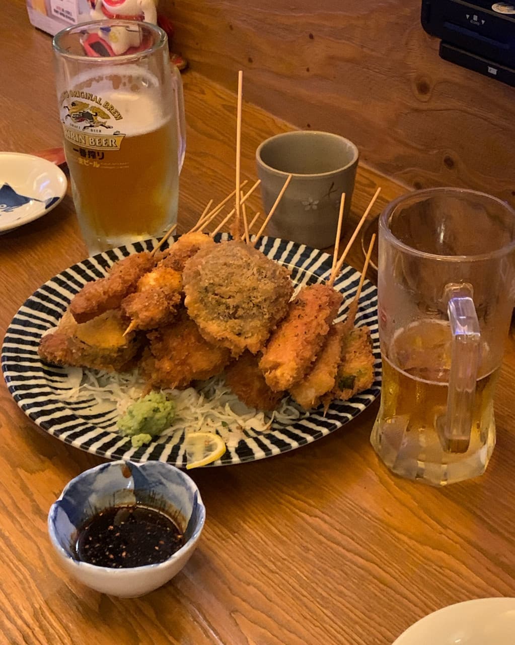 대구광역시 동구 요시쿠 신서 본점 대구 이자카야 나무 다찌석 위 바삭한 질감의 모듬 쿠시카츠와 생맥주. 노란 조명이 비치는 1인석에서 혼술을 즐기는 상황.