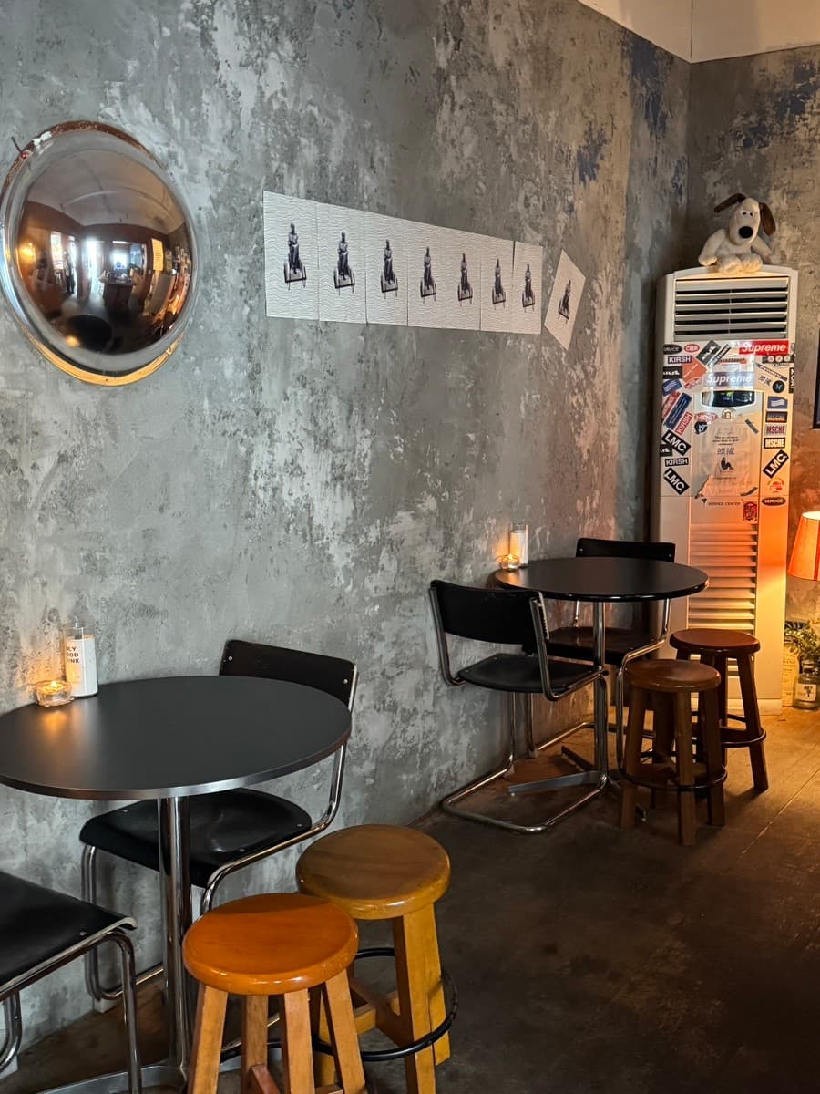 부산광역시 수영구 혼술 바(Bar) 표류 부산 - 노출 콘크리트 벽면 앞 원형 테이블과 1인석 스툴, 촛불 조명이 배치된 조용한 실내 구성