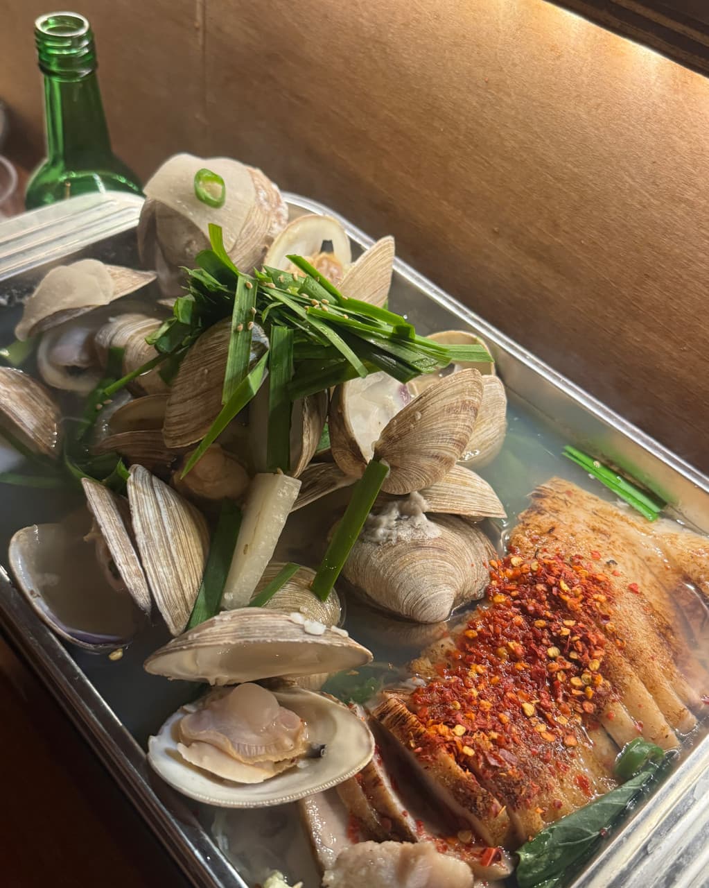 부산광역시 동래구 월하주방 부산 요리주점 다찌석 조명 아래 부추를 올린 조개찜과 고춧가루가 뿌려진 수육이 놓인 1인 혼술 차림
