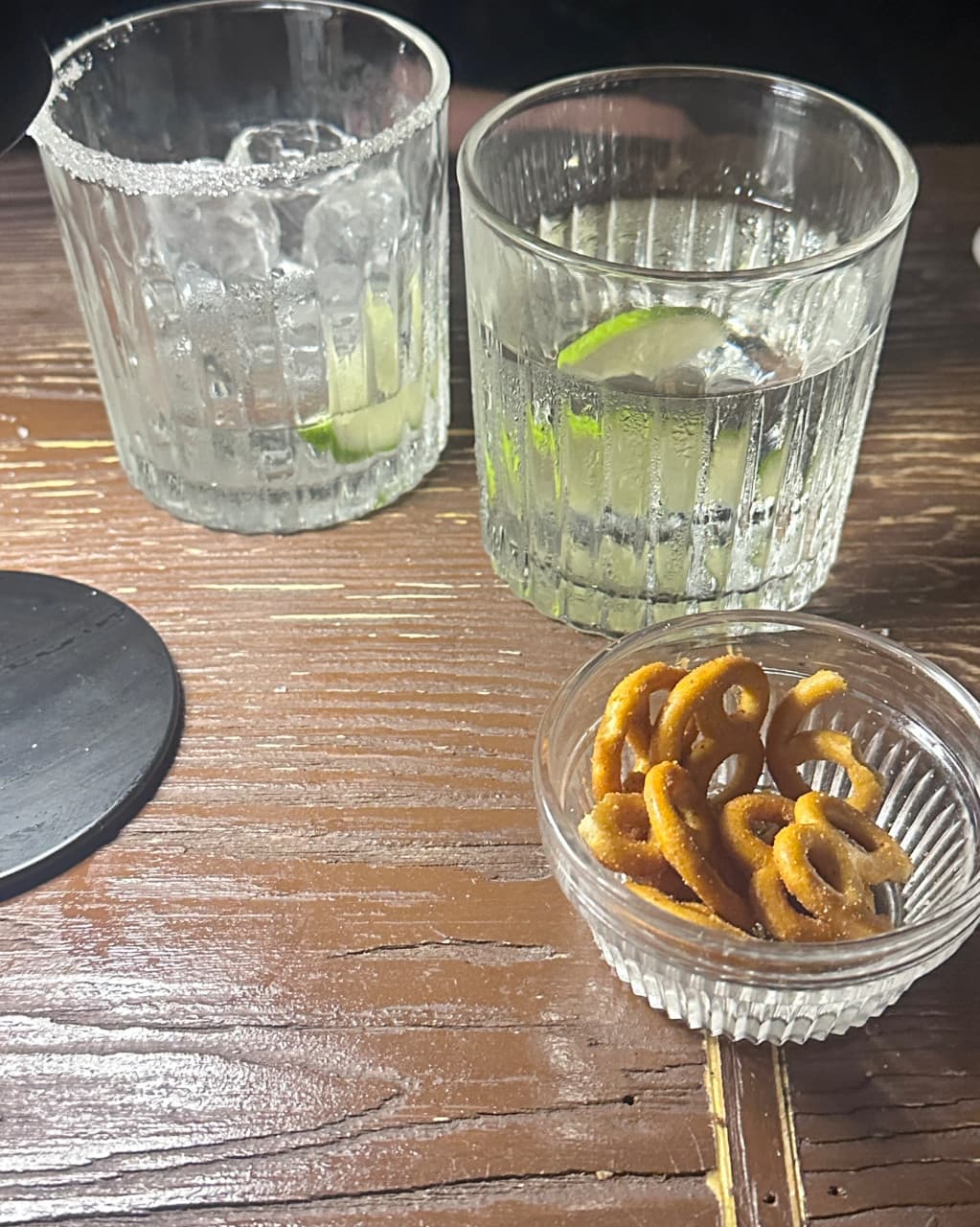 부산광역시 수영구 곁 부산혼술바 광안리점 바(Bar) 다찌석 나무 테이블 위 라임 조각이 든 칵테일과 프레첼. 소금이 묻은 잔과 얼음이 채워진 술잔이 놓인 1인 혼술 상황