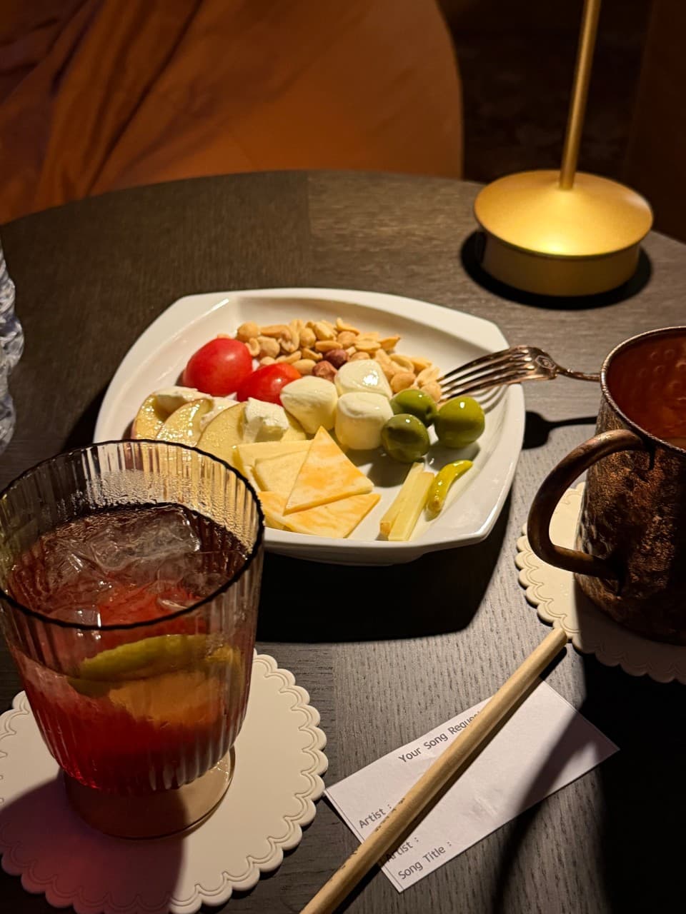 부산광역시 수영구 혼술 바(Bar) 광안리골방 부산 - 노란 조명 아래 치즈와 견과류 플레이트, 빨간 하이볼과 신청곡 메모지가 놓인 1인 테이블 상황