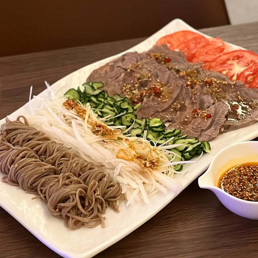 부산광역시 수영구 광안야행 부산 요리주점 다찌석 조명 아래 차려진 1인 혼술 안주. 소고기 수육과 메밀면, 오이, 토마토가 정갈하게 담긴 접시와 깨가 뿌려진 소스 종지.