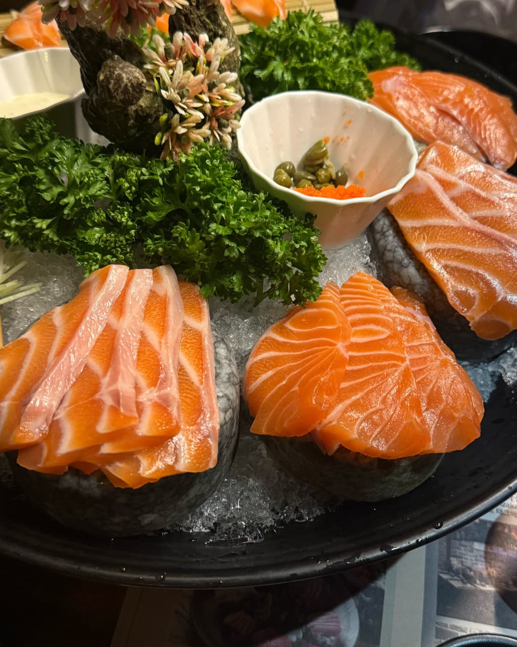 대전광역시 중구 이자카야 게다 대흥점 대전 다찌석 조명 아래 얼음 위 돌에 올려진 윤기 나는 1인 연어 사시미와 케이퍼가 담긴 혼술 세트.