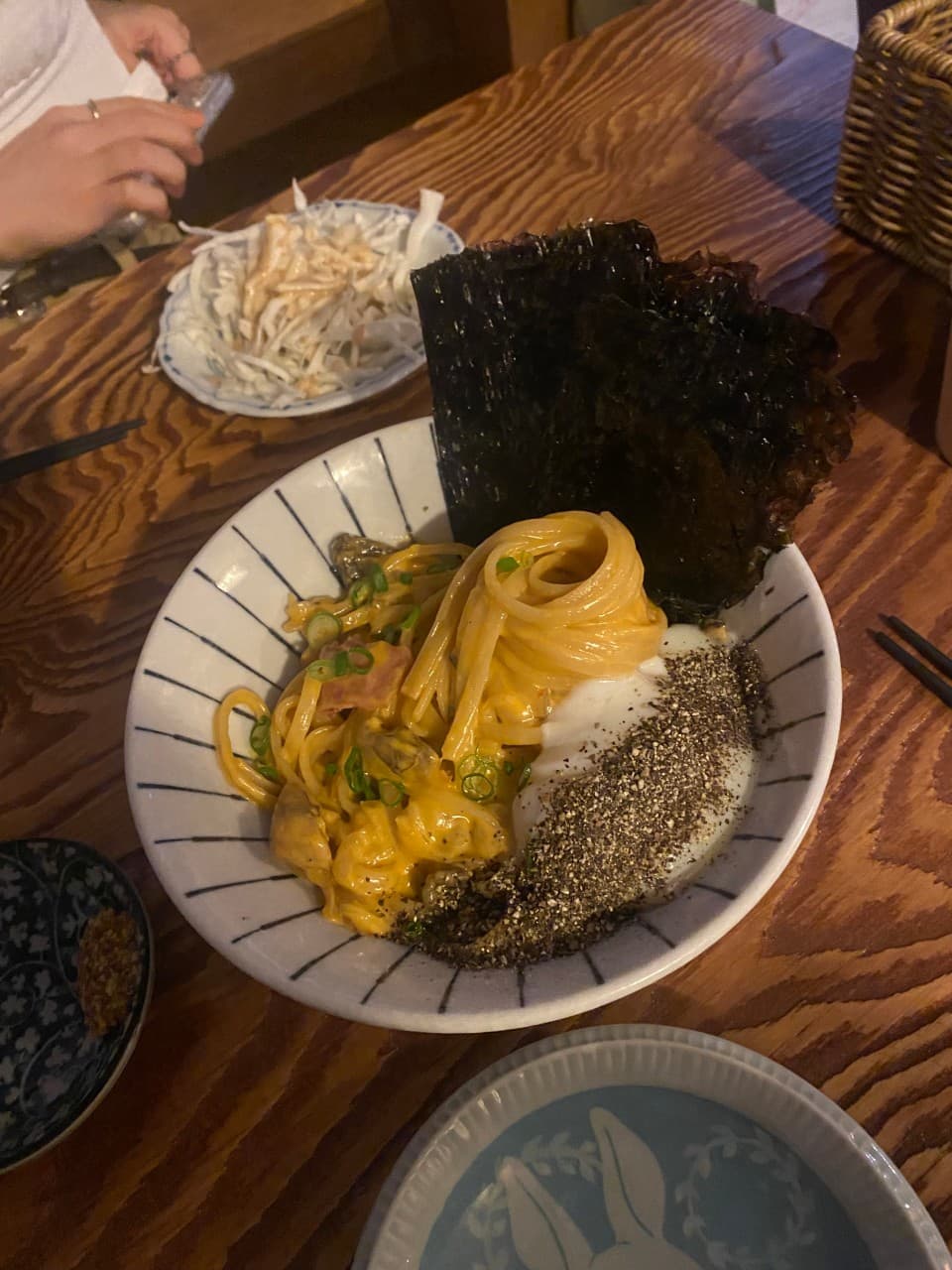 대전광역시 중구 요모 대전대흥점 이자카야 나무 다찌석 위 1인 면 요리. 김과 후추가 뿌려진 수란이 담긴 그릇과 나무 질감이 돋보이는 조명 아래 혼술 환경.