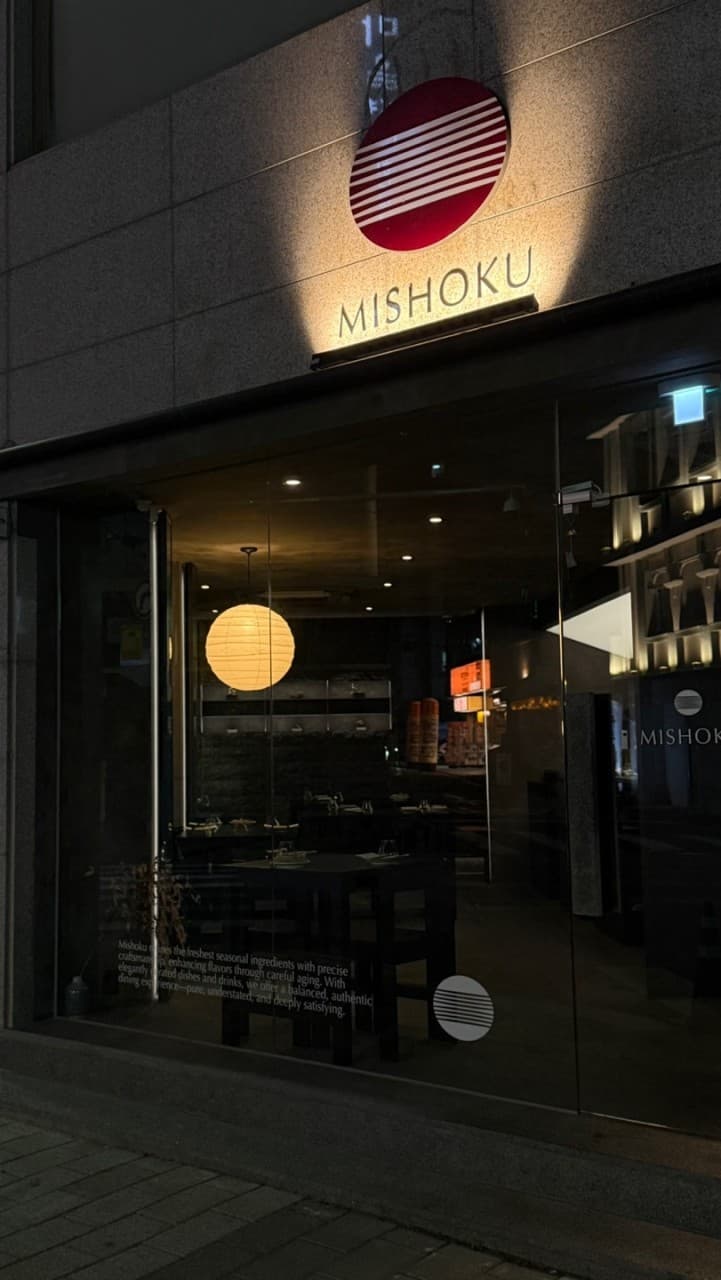 대전광역시 중구 이자카야 미쇼쿠 대전. 통유리창 너머 원형 전등과 검은색 테이블이 배치된 1인 다찌석 내부. 밤 시간대 조명 아래 혼술을 즐기는 정적인 식사 환경.