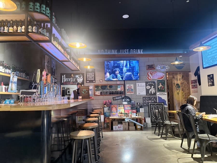 대전광역시 서구 크래프트피피 대전 맥주 호프 매장의 주황색 조명 아래 나열된 나무 다찌석과 맥주 탭. 1인 좌석과 다양한 포스터가 부착된 벽면의 혼술 공간.