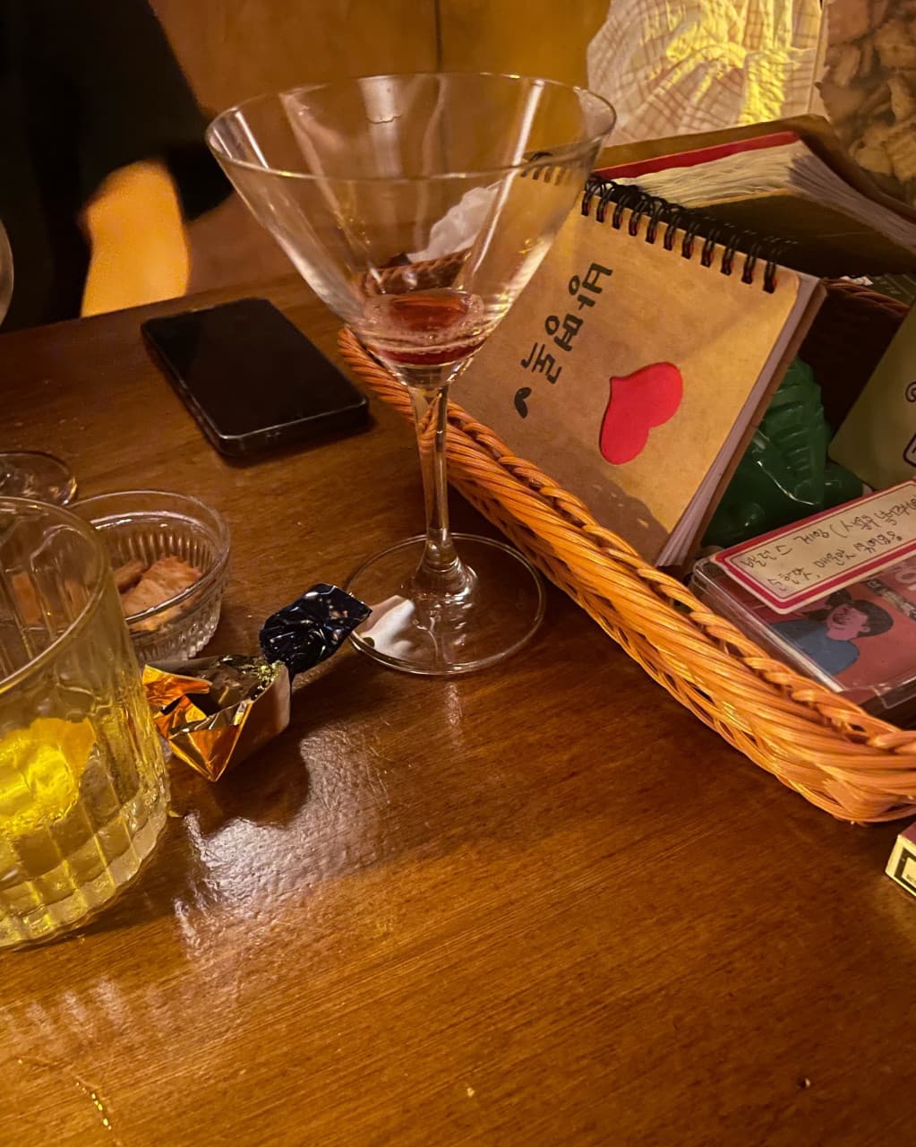 인천광역시 남동구 혼술바 고도 구월점 인천 바(Bar) - 주황빛 조명 아래 나무 다찌석에 놓인 칵테일과 방명록이 있는 1인 혼술 상황