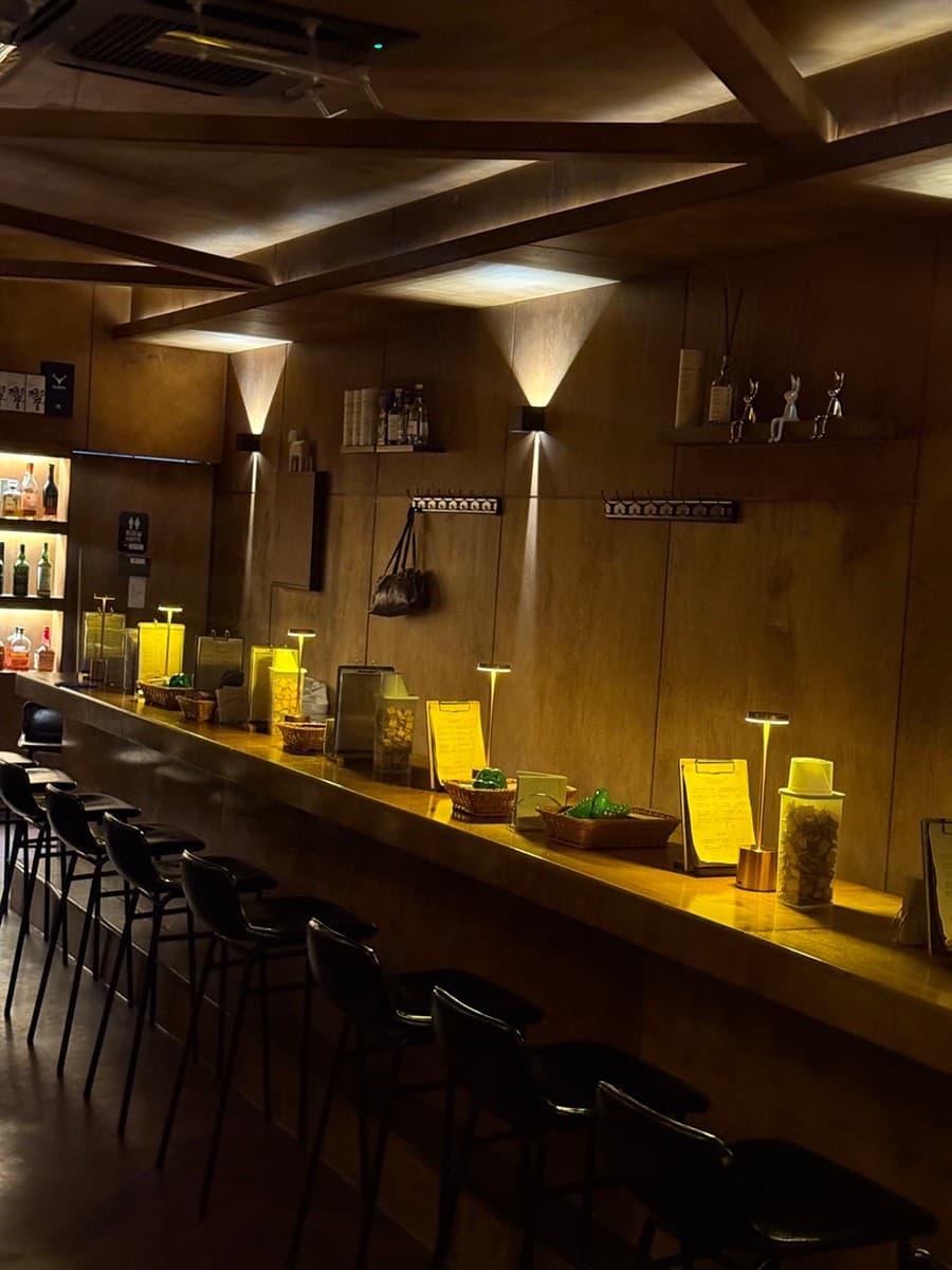인천광역시 남동구 혼술바 고도 구월점 인천 바(Bar)의 노란 조명 아래 긴 원목 다찌석과 1인 좌석. 개별 스탠드가 배치되어 혼술을 즐기는 상황을 보여줌.