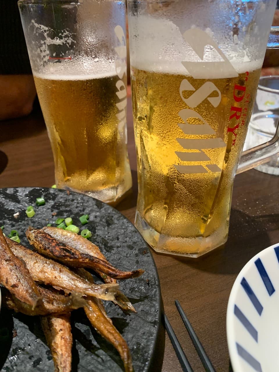 인천광역시 남동구 이자카야 야키토리동작 인천시청점 다찌석 위 생맥주와 노릇한 시샤모 구이. 조명이 비치는 맥주잔의 물방울과 구워진 생선 질감이 강조된 1인 혼술 차림.