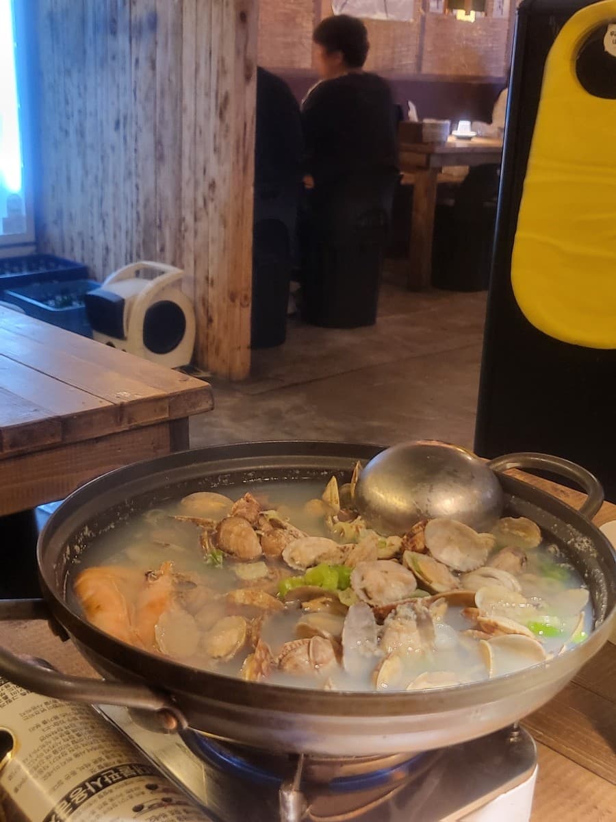 인천광역시 남동구 한식주점낭만 구월점 인천 요리주점. 나무 칸막이 다찌석과 가스버너 위 조개와 새우가 담긴 맑은 탕. 낮은 조명 아래 1인 혼술 위주로 배치된 테이블 상황.