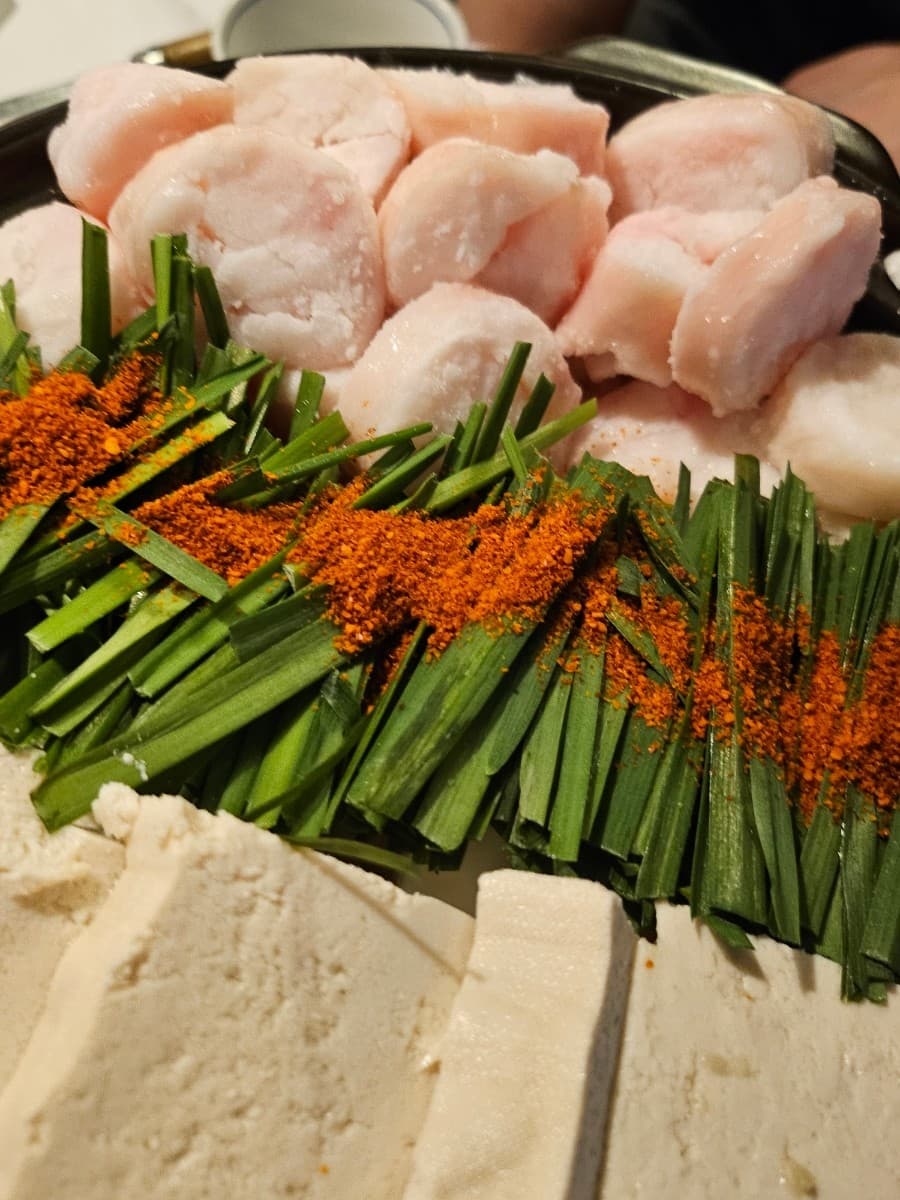 인천광역시 부평구 이자카야 아이다가라 부평 인천 1인 다찌석 조명 아래 대창과 부추, 고춧가루가 뿌려진 모츠나베. 혼술 상황의 식재료 질감이 강조된 구성.