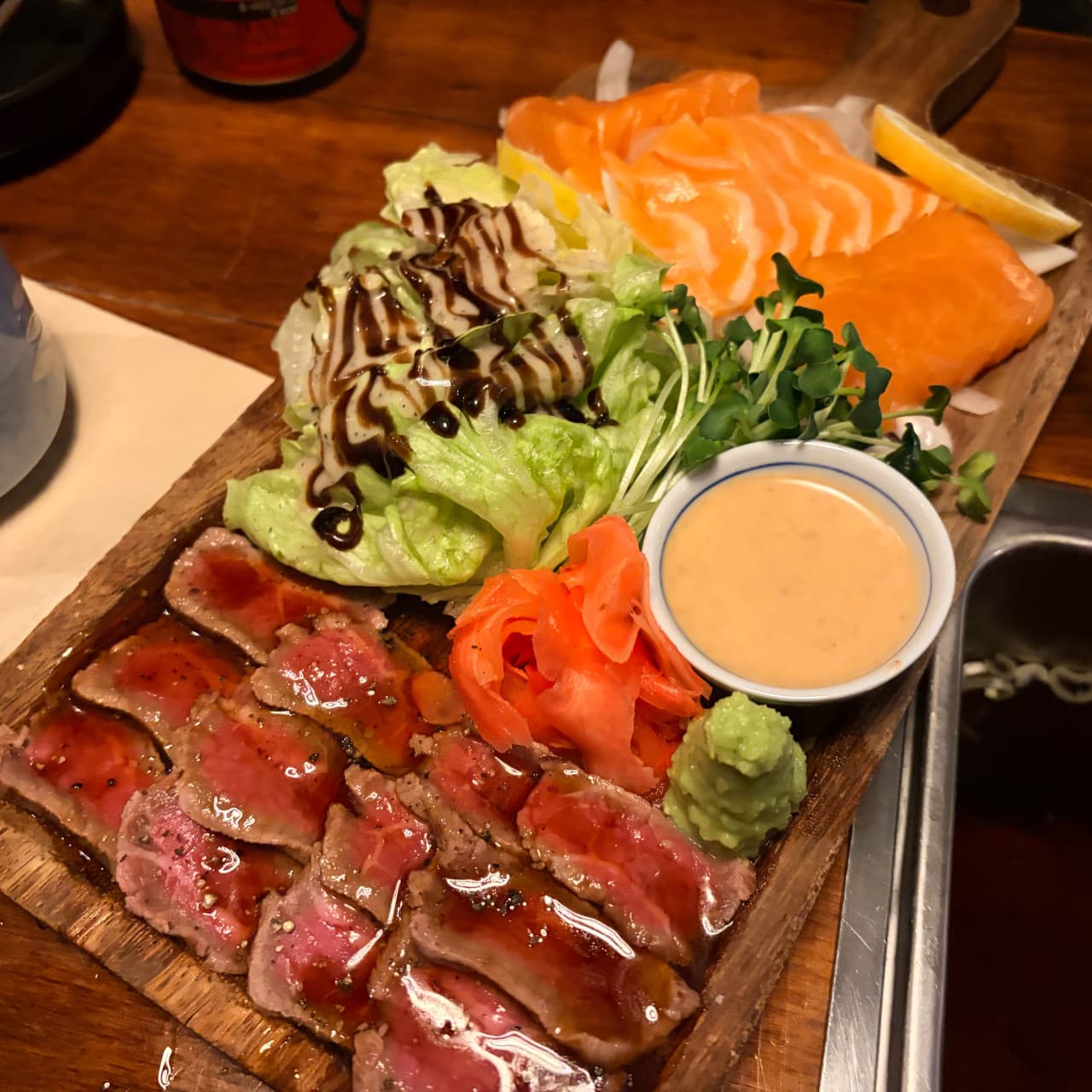 인천광역시 연수구 요리주점 철길부산집 송도타임스페이스점 인천. 나무 도마 위 연어와 소고기 타다끼가 놓인 다찌석 혼술 상황. 낮은 조명과 정갈한 음식의 질감이 돋보임.