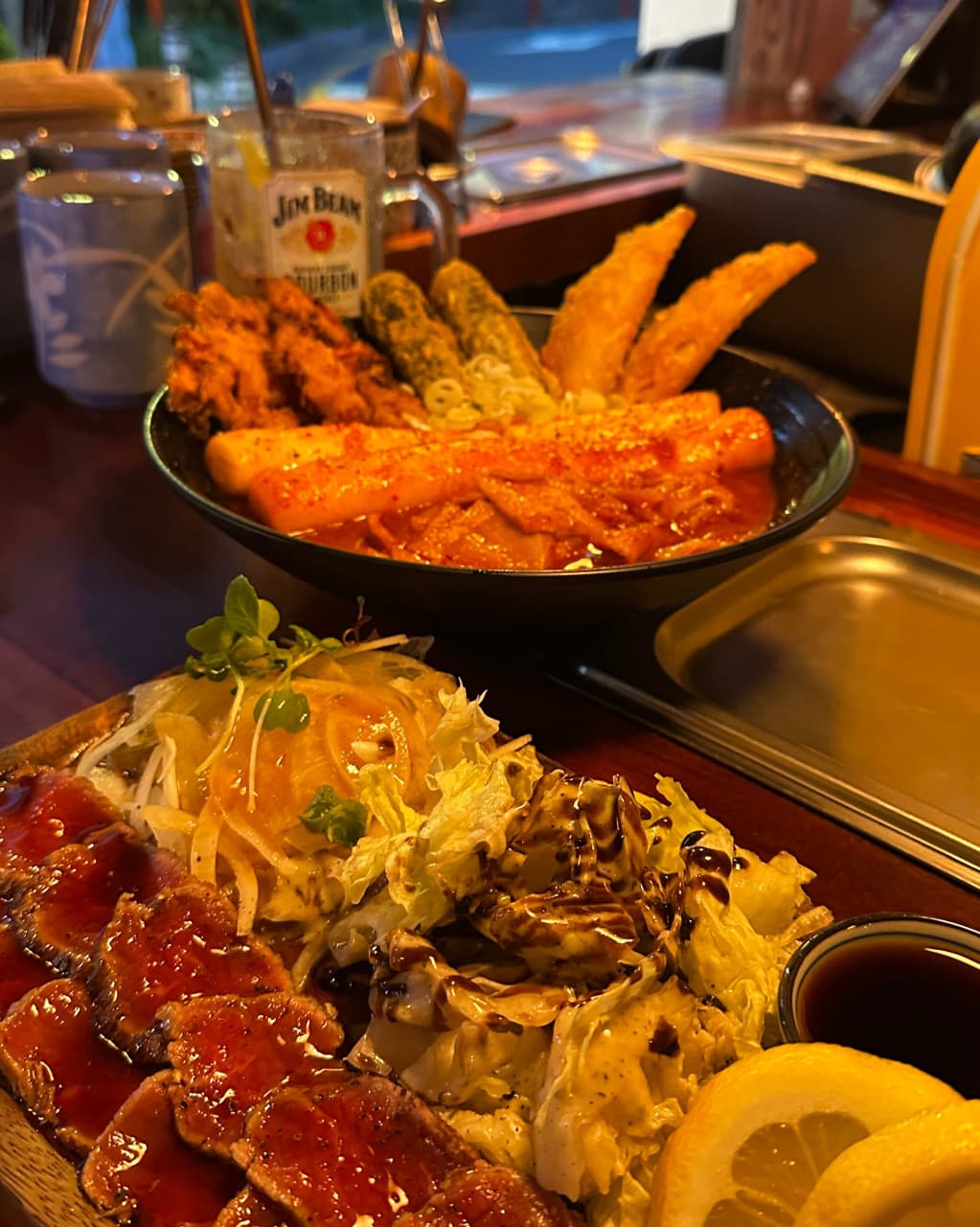 인천광역시 연수구 요리주점 철길부산집 송도타임스페이스점 인천 다찌석 1인 혼술. 소고기 타다끼와 가래떡 떡볶이, 모둠 튀김이 놓인 나무 테이블 위 황색 조명이 비치는 상황.