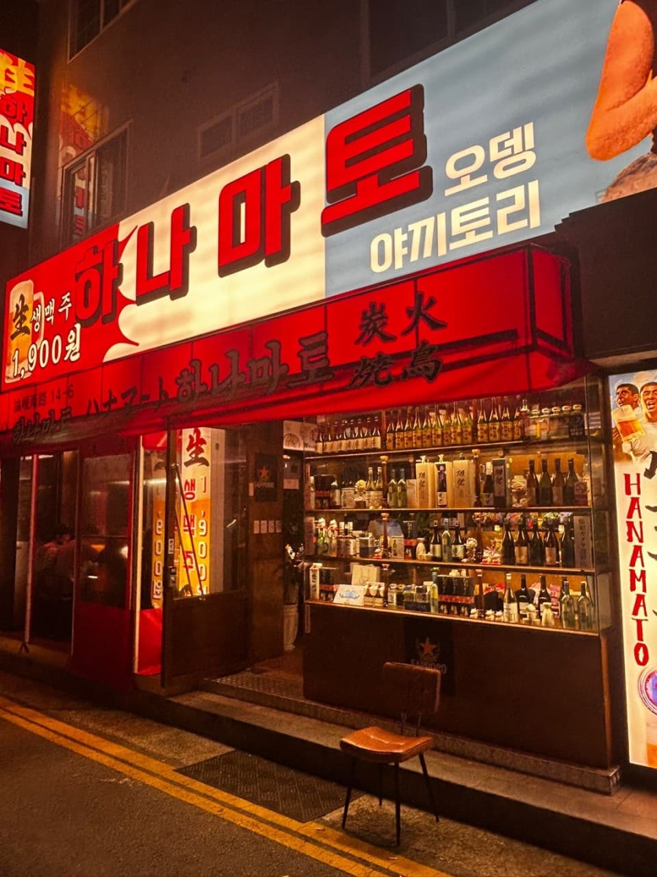 인천광역시 남동구 혼술 요리주점 하나마토 인천논현 - 붉은 조명 아래 진열된 사케 병들과 입구 앞 1인용 의자가 배치된 외관