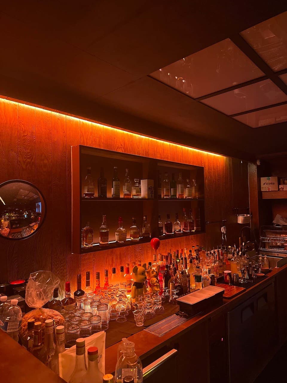 제주특별자치도 제주시 단지 제주혼술바 바(Bar)의 주황색 조명이 비치는 목재 벽면과 위스키 진열장. 다찌석 카운터에 나열된 유리잔과 1인 혼술객을 위한 공간 구성.