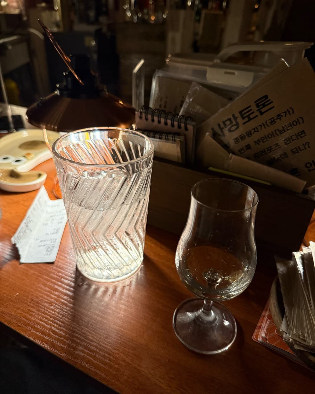 제주특별자치도 제주시 곁 제주혼술바 탑동점 본점 바(Bar). 낮은 조명 아래 다찌석 위 투명한 유리잔과 물잔이 놓인 1인 혼술 상황.