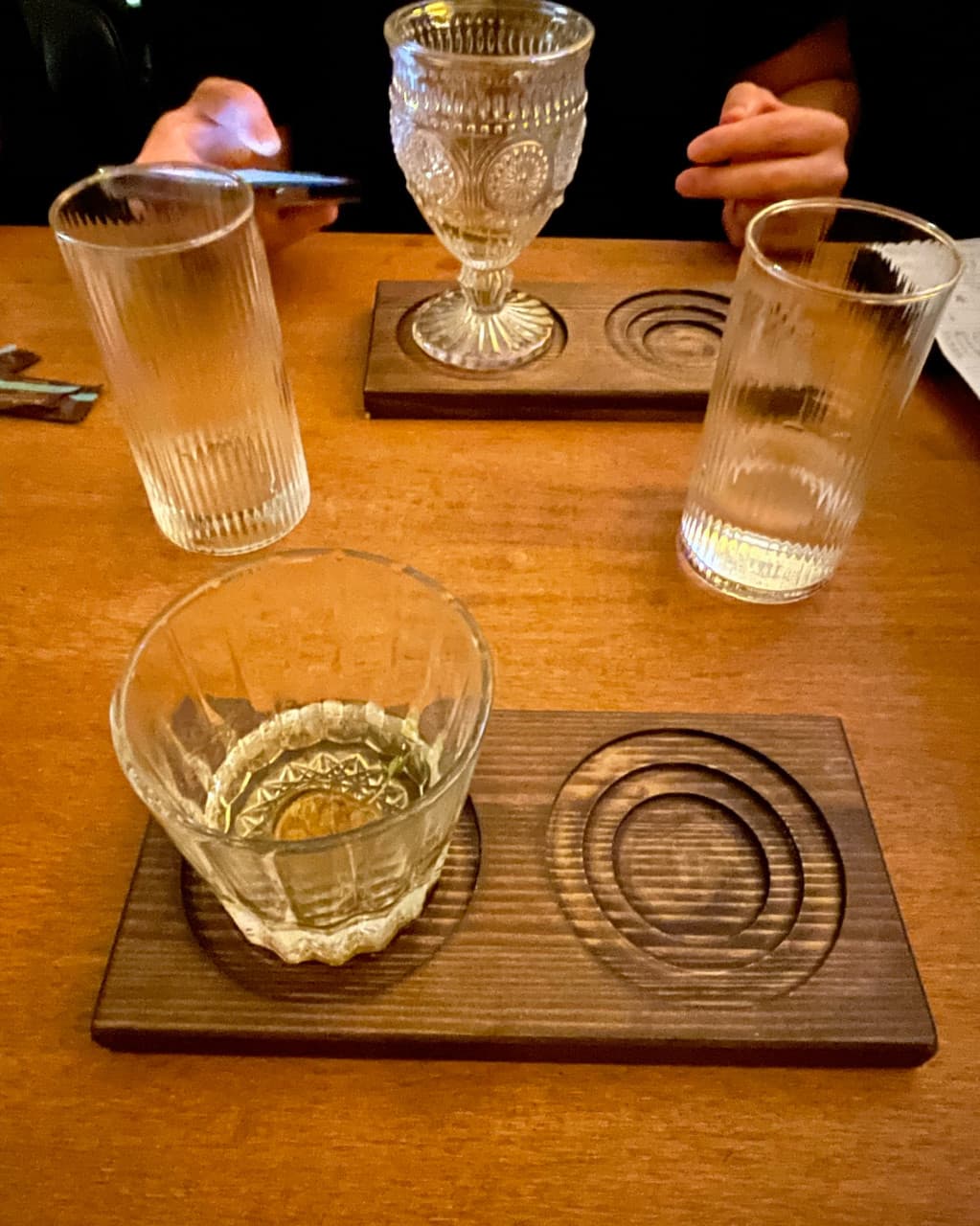 제주특별자치도 서귀포시 자유의지 혼술바 제주서귀포점 바(Bar) - 주황색 조명 아래 나무 테이블 위 투명한 음료가 담긴 크리스탈 잔과 나무 받침. 1인 다찌석에 앉아 혼술 중인 상황