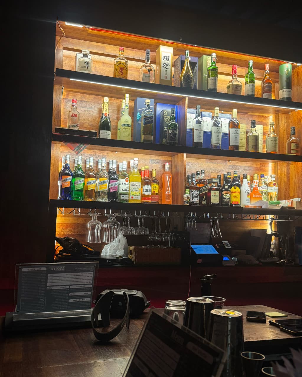 제주특별자치도 서귀포시 제주혼술바 언스테이블 서귀포점 바(Bar). 진열장의 노란 조명과 여러 종류의 술병, 다찌석 메뉴판이 보이는 1인 혼술 환경.