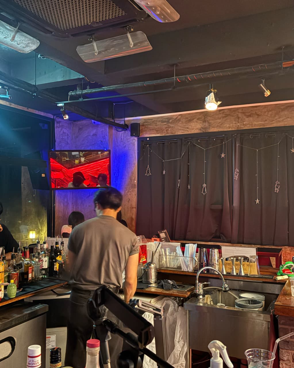 제주특별자치도 서귀포시 제주혼술바 언스테이블 서귀포점 바(Bar) 다찌석 혼술. 상단 조명과 블루 네온 아래 술병이 가득한 카운터 공간과 바텐더가 서 있는 상황