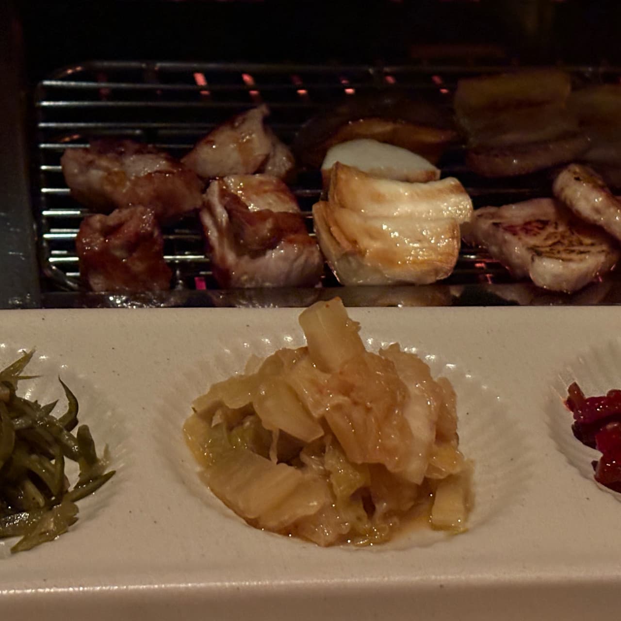 제주특별자치도 서귀포시 명단 BBQ BAR 제주 혼술 - 조명 아래 석쇠 위 고기와 버섯, 세 가지 밑반찬이 차려진 1인 다찌석 구성의 기타 요리 전문점