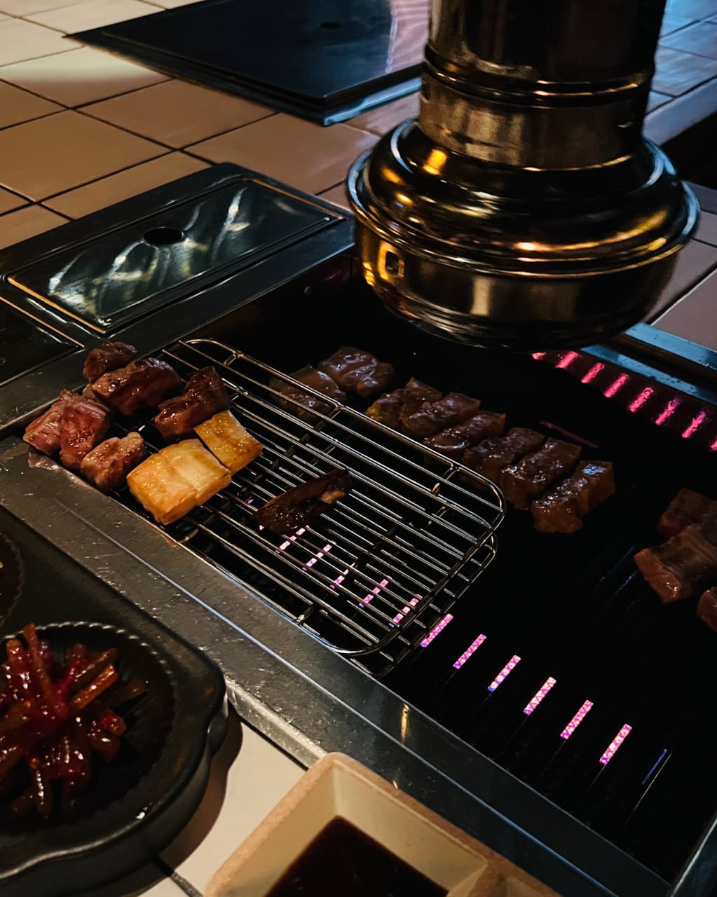 제주특별자치도 서귀포시 명단 BBQ BAR 제주 다찌석 1인 화로구이. 어두운 조명 아래 붉은 숯불 위로 익어가는 고기 질감과 환기구가 보이는 기타 구이 전문점 분위기.