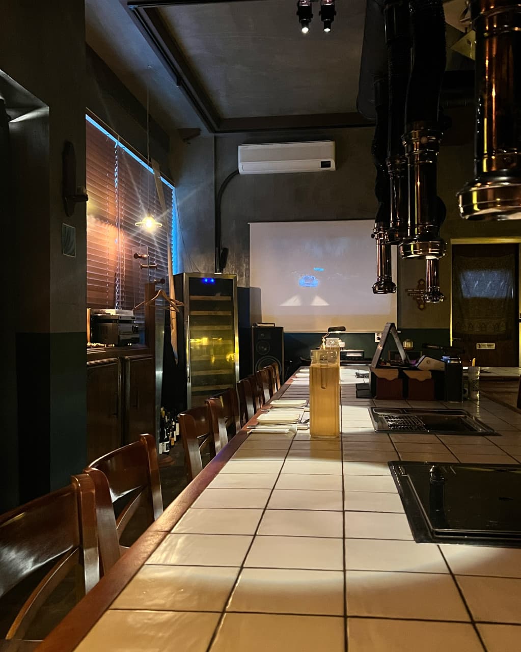 제주특별자치도 서귀포시 혼술 명단 BBQ BAR 제주 - 1인 다찌석과 개인 화로가 마련된 기타 BBQ 매장. 화이트 타일 테이블과 상단 배기 후드가 배치된 낮은 조도의 내부 공간.