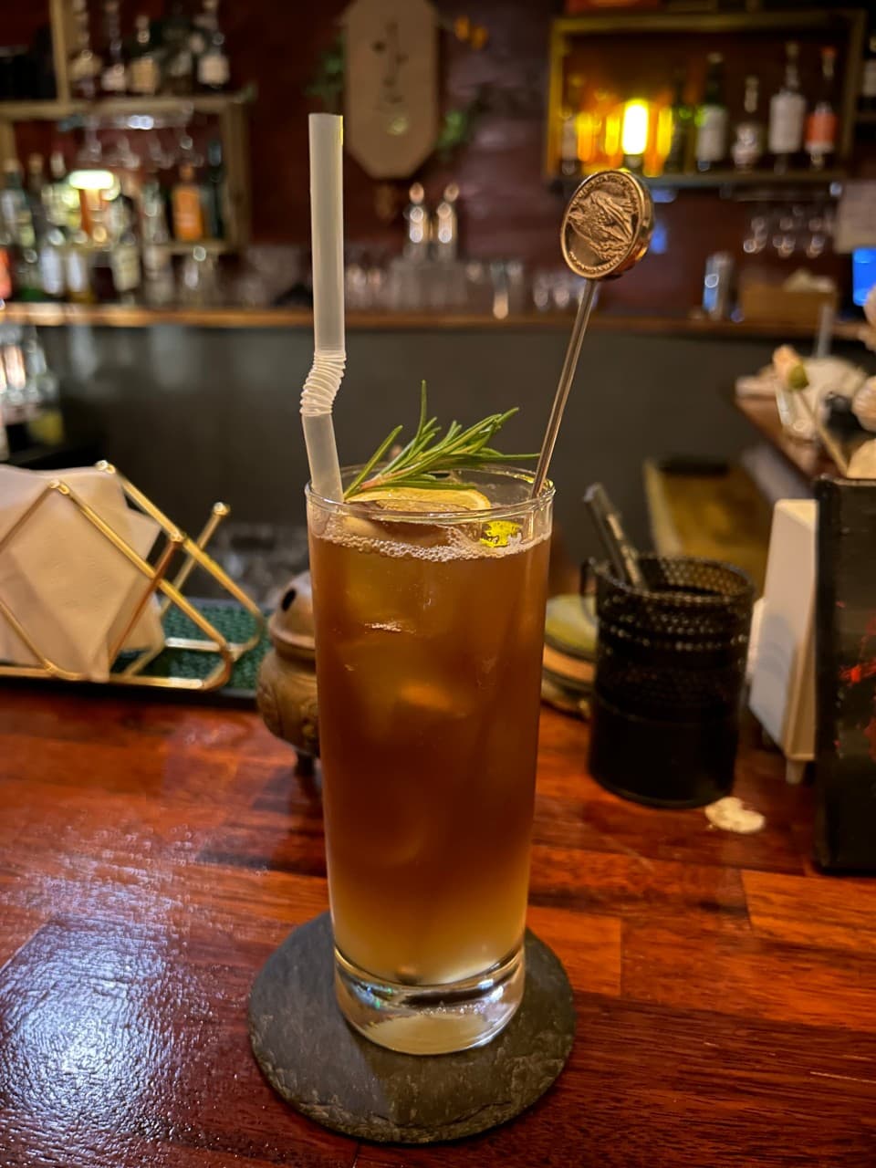 제주특별자치도 제주시 제주아홉 혼술바 본점 협재점 바(Bar)의 나무 다찌석. 로즈마리와 레몬 슬라이스가 담긴 1인 혼술용 칵테일이 노란 조명 아래 놓인 상황