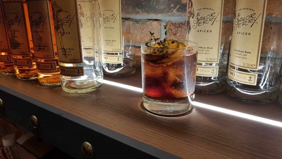 제주특별자치도 서귀포시 제리스펍 제주서귀포점 맥주 호프 다찌석 선형 조명 위 라임과 허브가 담긴 1인 칵테일과 세일러제리 럼 병들이 나열된 혼술 현장
