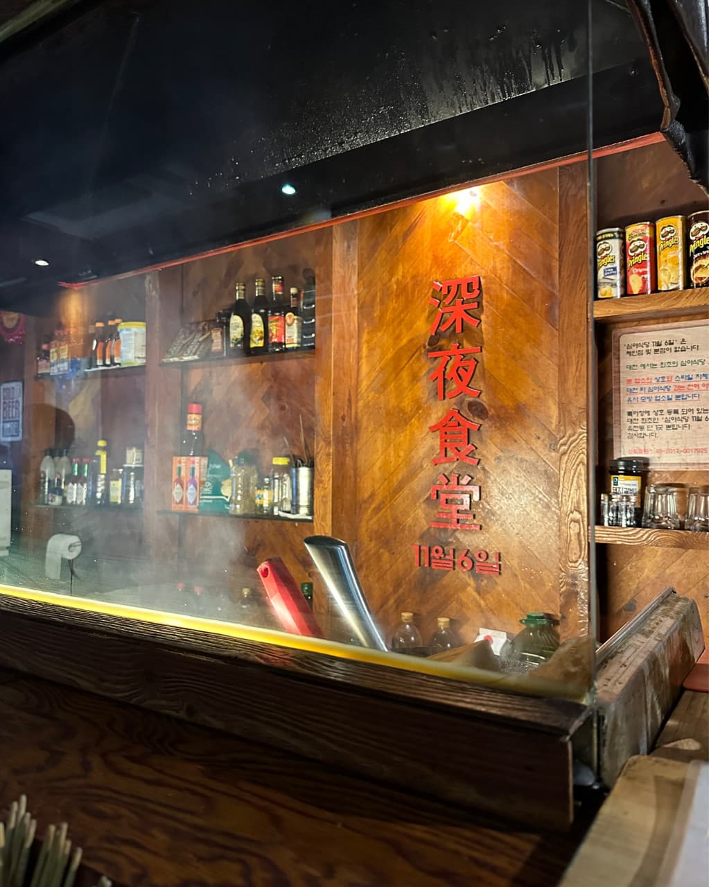 대전광역시 중구 심야식당11월6일 대전 다찌석. 주황빛 조명 아래 나무 벽면과 선반 위 식재료가 비치는 김 서린 유리창 앞 1인 혼술 공간.