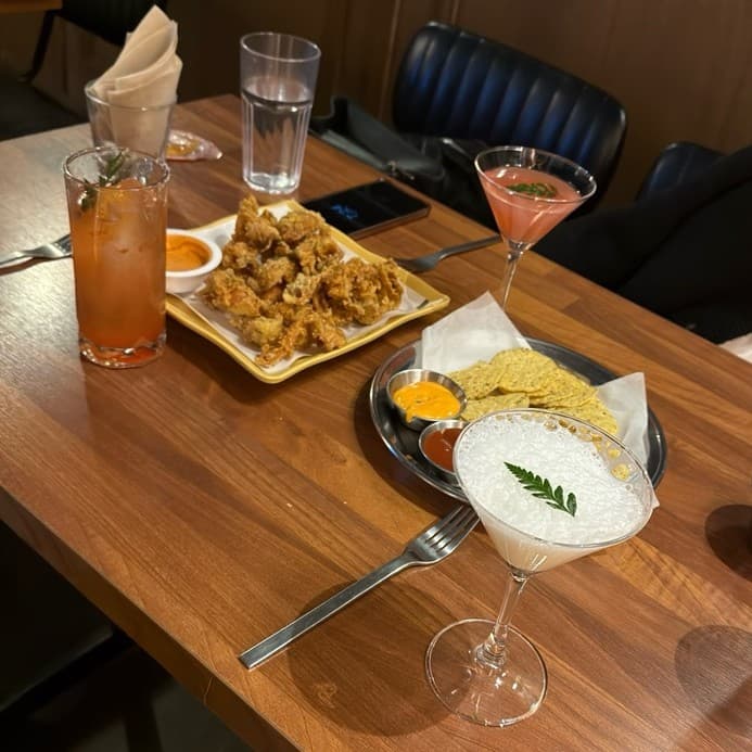대전광역시 동구 공강 대전 바(Bar) 원목 테이블 위 칵테일과 튀김 안주. 조명 아래 혼술 좌석에 차려진 바삭한 나초와 거품 가득한 음료.