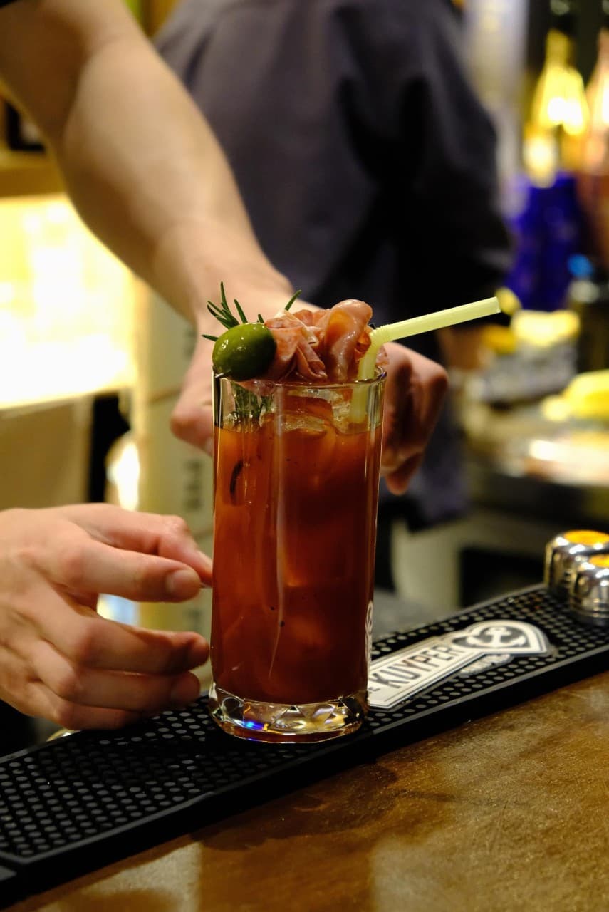 대전광역시 동구 공강 대전 바(Bar) 다찌석 1인 칵테일. 올리브와 하몽 가니시가 올라간 붉은 음료가 노란 조명 아래 나무 테이블 위에 놓인 혼술 상황.