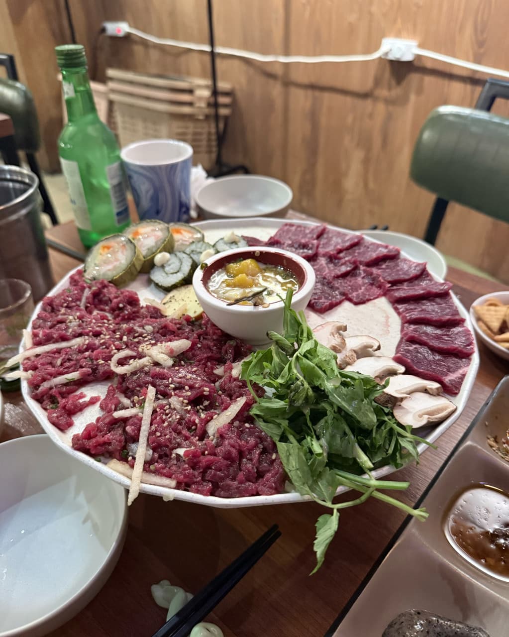 경기도 안산시 반월가 경기 요리주점 - 나무 인테리어 아래 1인 혼술 다찌석에 차려진 선홍빛 육회와 뭉티기, 김밥이 담긴 정갈한 접시와 소주 한 병