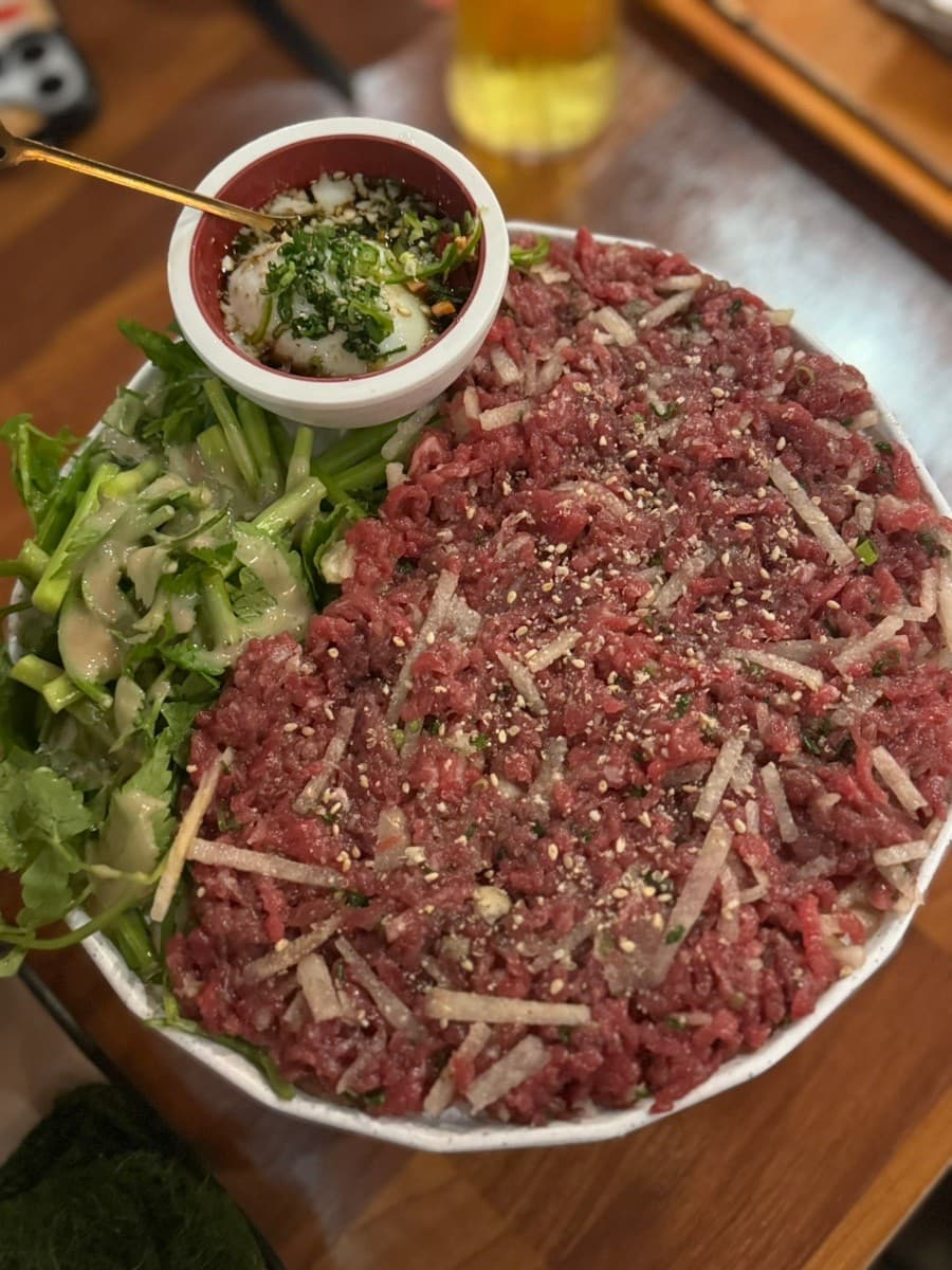 경기도 안산시 요리주점 반월가 경기 나무 다찌석에 차려진 붉은 육회와 수란 소스. 1인 혼술 상황에 맞춰 주류와 함께 놓인 안주의 구성과 질감을 조명 아래서 포착.