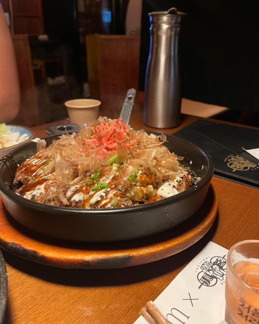 경기도 성남시 이자카야 잔잔 정자역점 경기 나무 테이블 위 가쓰오부시가 듬뿍 올라간 오코노미야키. 조명 아래 다찌석에서 혼술을 하는 1인용 상차림 상황.