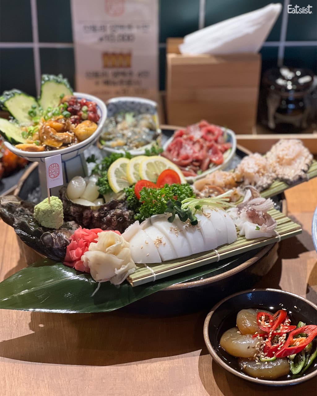경기도 고양시 이자카야 일월육일 일산점 경기 다찌석 조명 아래 놓인 1인 해산물 한 상. 오징어와 전복, 멍게의 촉촉한 질감이 드러나는 목재 테이블 위 혼술 상황.
