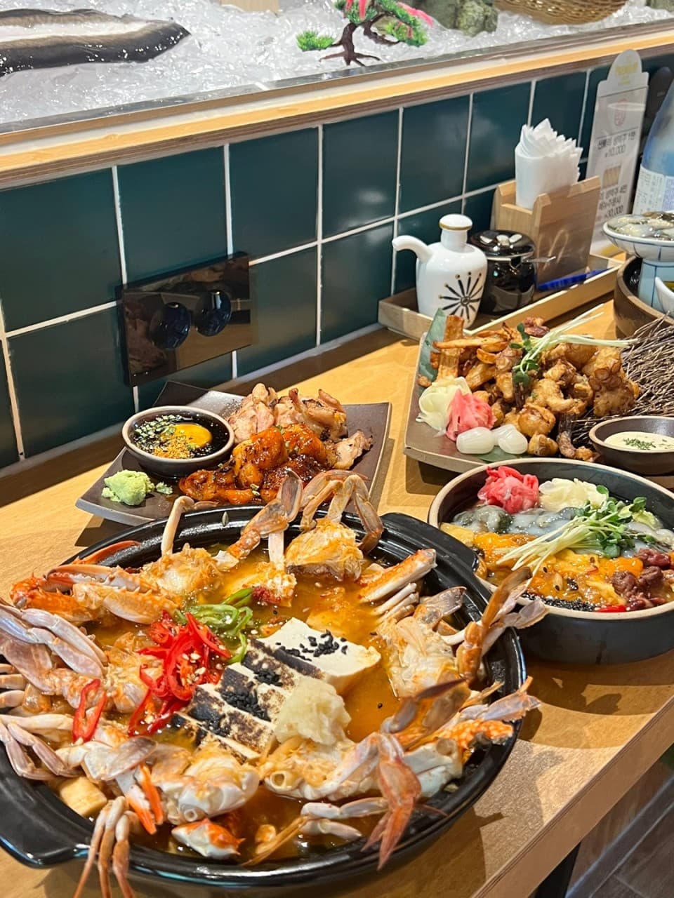경기도 고양시 이자카야 일월육일 일산점 경기 다찌석. 조명 아래 꽃게탕과 우니, 튀김이 차려진 나무 테이블. 녹색 타일 배경의 1인석에서 혼술을 즐기는 상황.