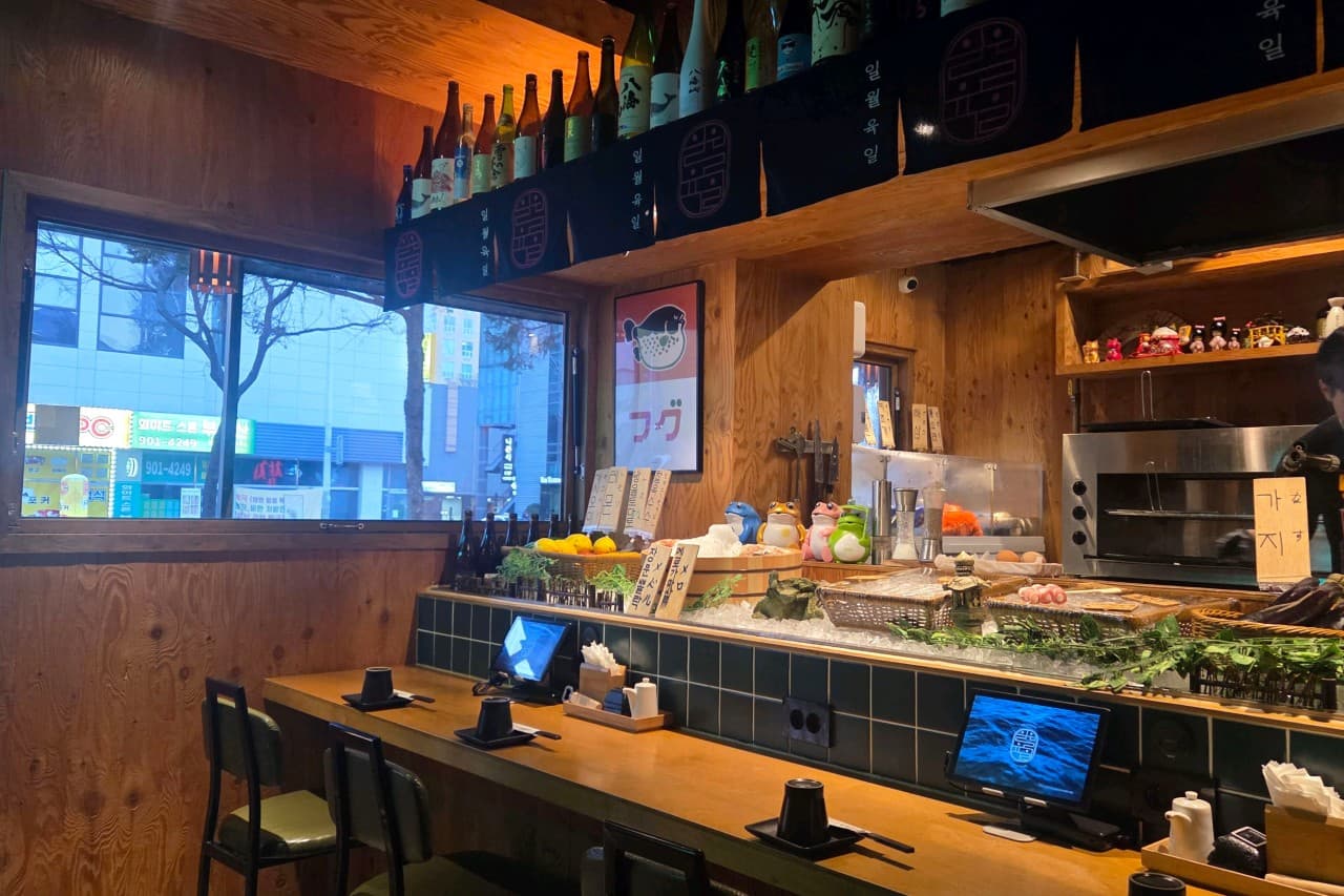 경기도 고양시 이자카야 일월육일 일산점 경기 다찌석과 1인 전용 태블릿. 따뜻한 조명 아래 얼음 위 식재료가 진열된 나무 카운터에서 혼술을 즐기는 상황.