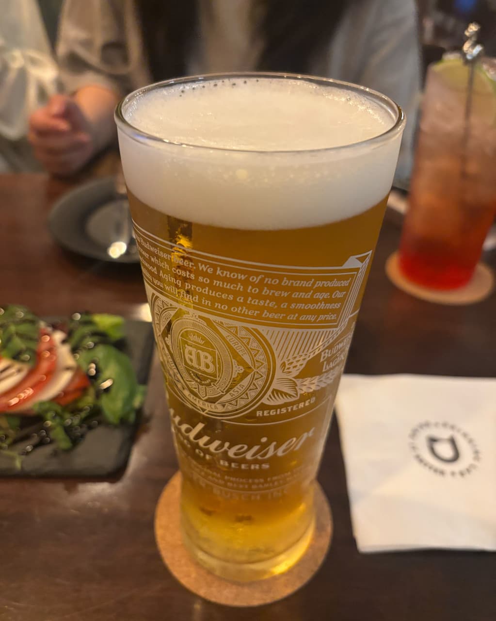 경기도 화성시 드링킹랩 경기 바 혼술 1인석. 거품이 가득한 생맥주와 발사믹 드레싱을 얹은 카프레제 샐러드가 차려진 조명 아래 나무 테이블 풍경.