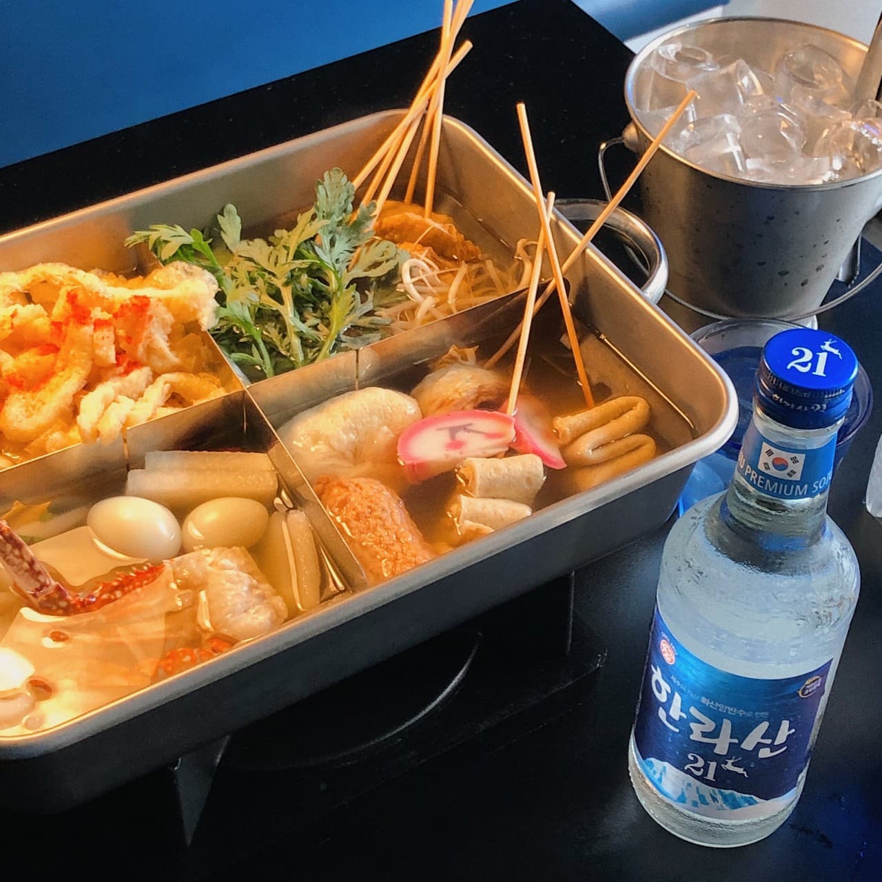 경기도 용인시 요리주점 바차 수지점 경기 다찌석에서 푸른 조명 아래 김이 나는 모둠 오뎅탕과 차가운 한라산 소주를 즐기는 1인 혼술 상황