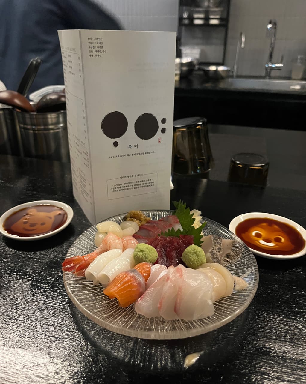 경기도 하남시 옥여 경기 다찌석에 차려진 1인 사시미와 캐릭터 간장 종지. 기타 주점의 조명 아래 선명한 회의 질감이 드러나는 혼술 상황.