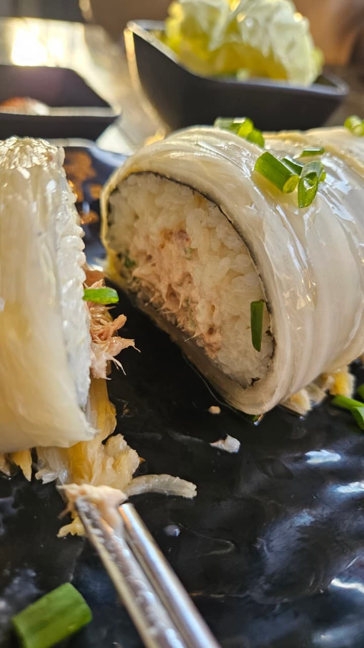 경기도 평택시 요리주점 편지 본점 경기 다찌석 조명 아래 차려진 혼술 1인 안주 묵은지 말이. 윤기 흐르는 배추 속 꽉 찬 참치와 밥의 질감이 검은 접시 위에서 선명하게 보임.