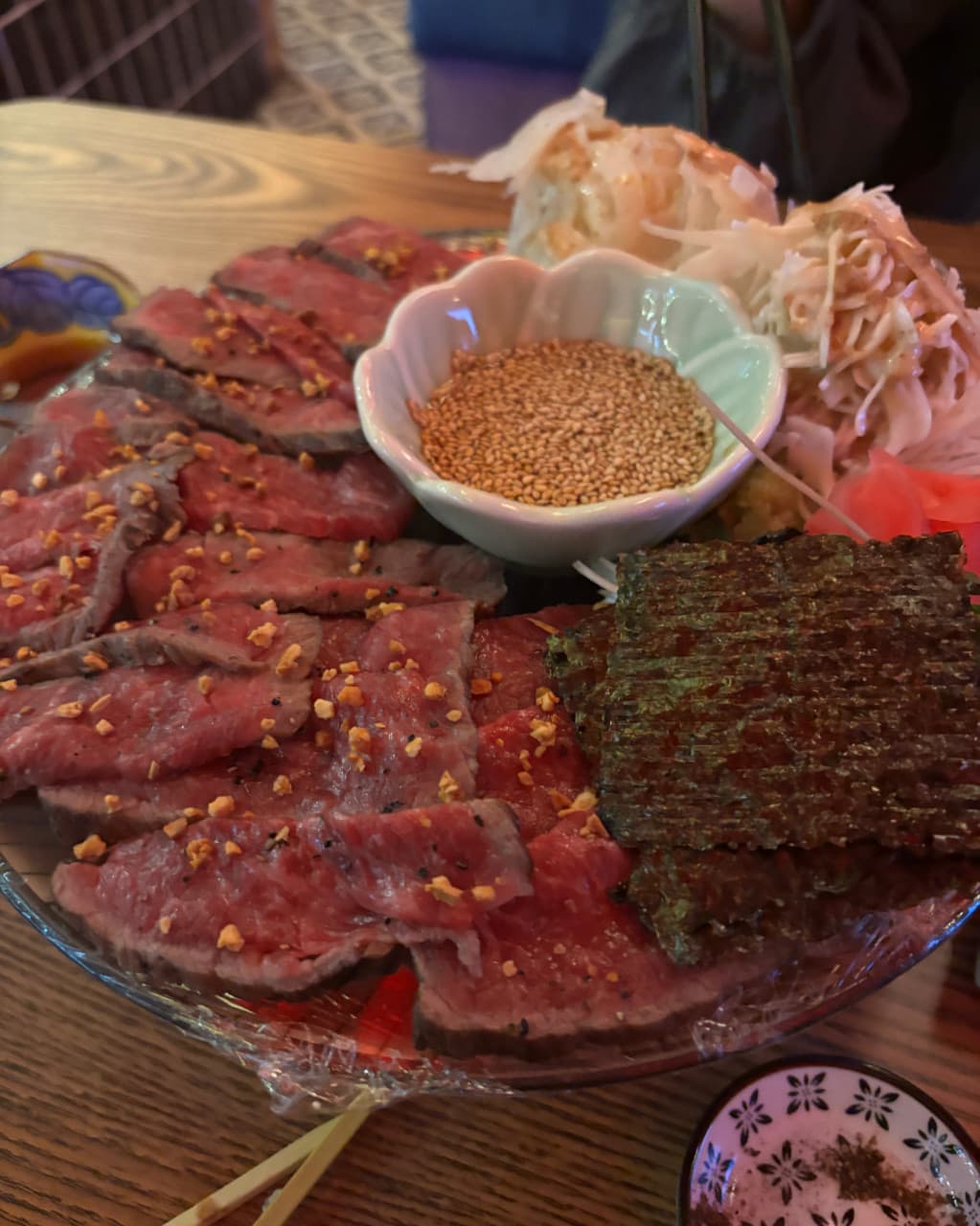 경기도 안산시 숯토리 안산고잔점 경기 이자카야 다찌석 혼술. 붉은 소고기 타다키와 김, 양파 슬라이스가 담긴 접시가 어두운 조명 아래 나무 테이블에 놓인 모습.