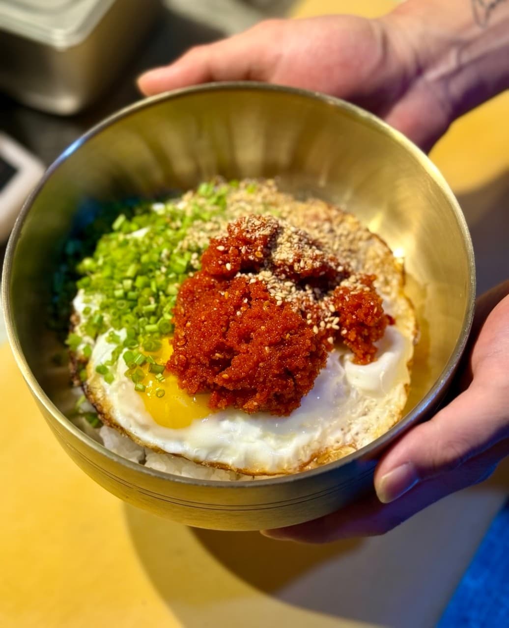 대구광역시 달서구 영남막회초장 상인본점 대구의 조명 아래 놋그릇에 담긴 계란 프라이와 양념 덮밥. 다찌석에서 혼술로 즐기는 1인 메뉴의 붉은 양념 질감이 강조된 기타 식당의 상황.