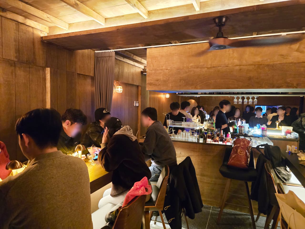 대구광역시 중구 블렌딩바 대구혼술바 교동점 바(Bar). 노란 조명이 비치는 나무 소재 카운터석에서 1인 손님들이 혼술을 즐기며 바텐더가 투명한 유리잔에 칵테일을 담아내는 상황.