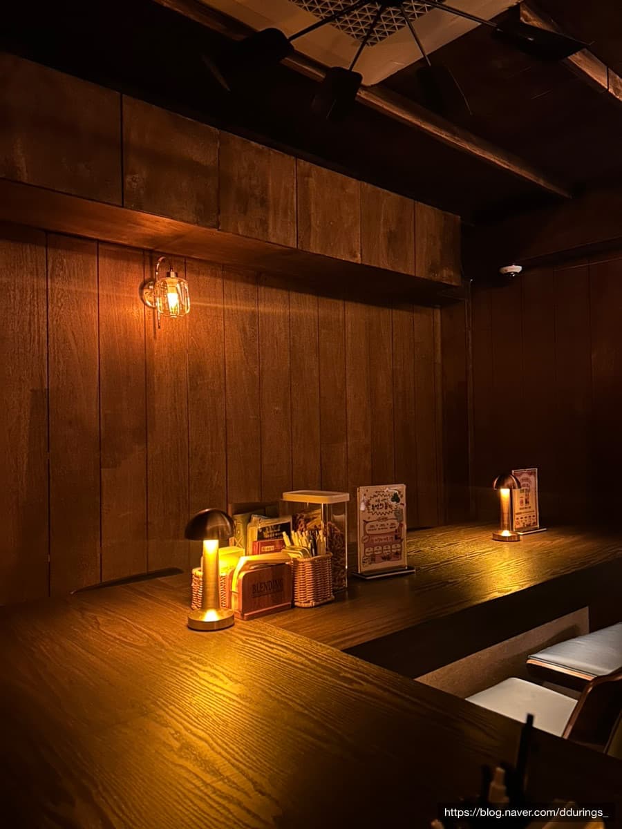 대구광역시 중구 블렌딩바 대구혼술바 교동점 바(Bar)의 어두운 우드 다찌석과 1인 좌석. 주황색 테이블 조명 아래 메뉴판과 소품이 배치된 혼술 전용 공간임.