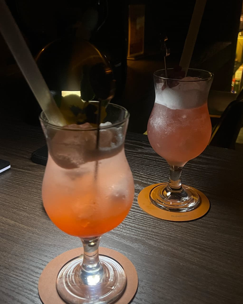 대구광역시 중구 블렌딩바 대구혼술바 교동점 바(Bar) 다찌석에 놓인 분홍빛 칵테일. 어두운 배경 속 핀 조명이 비추는 유리잔과 얼음의 질감으로 표현된 1인 혼술 분위기