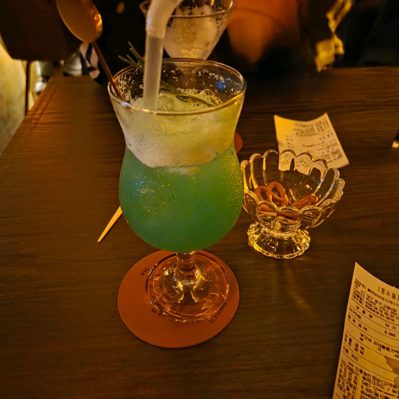 대구광역시 중구 블렌딩바 대구혼술바 교동점 바(Bar)의 주황빛 조명 아래 초록색 칵테일과 프레첼. 나무 소재 다찌석에서 혼술을 즐기는 상황.