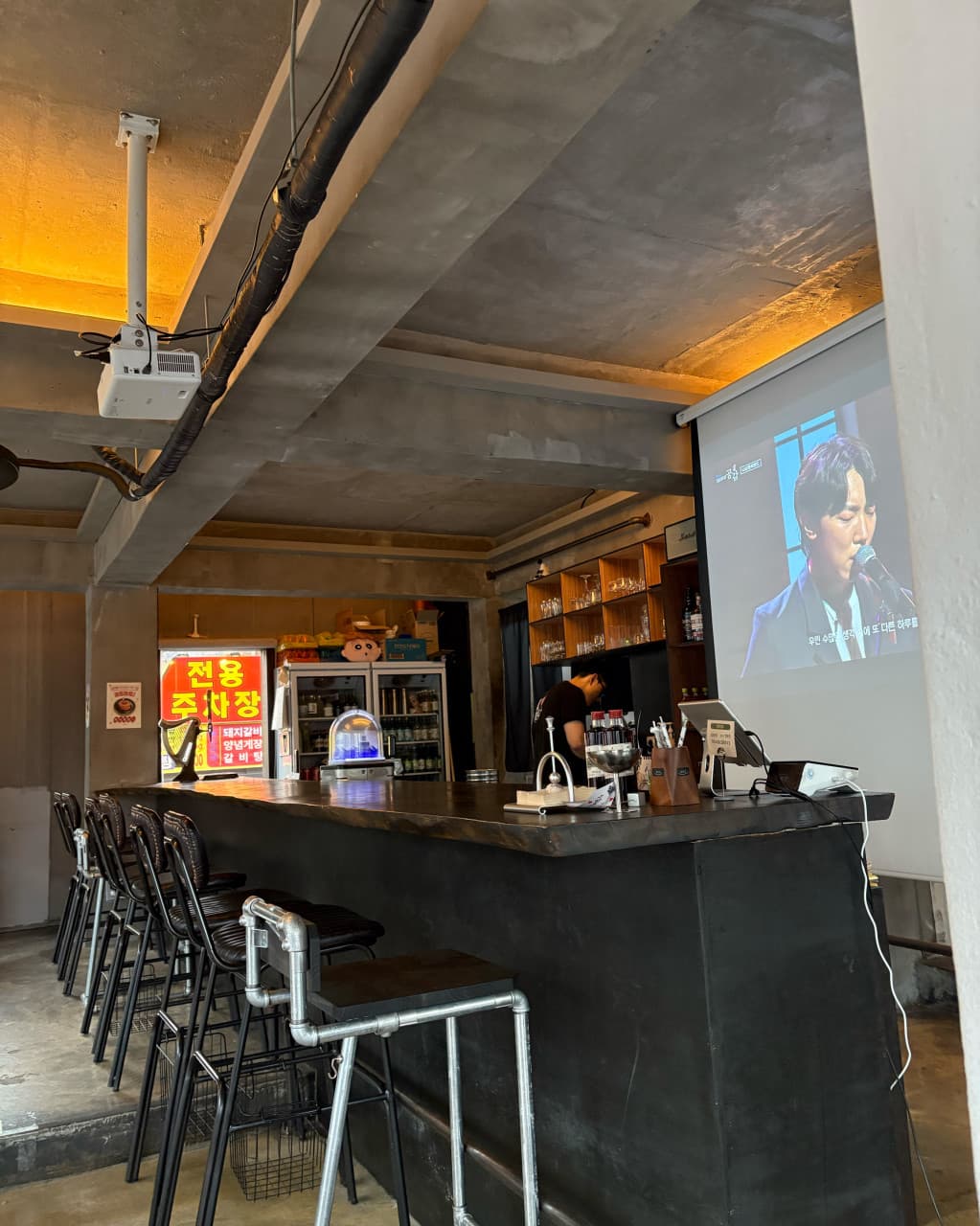 대구광역시 북구 새로나 대구의 황색 조명이 비치는 다찌석과 1인용 의자. 빔프로젝터 영상이 상영되는 공간에서 혼술을 즐기는 기타 카테고리의 매장 내부 전경.
